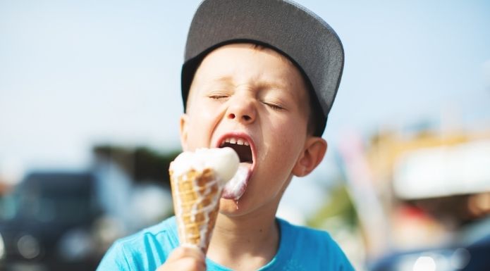 Young boy eating ice cream quickly, risking a brain freeze,