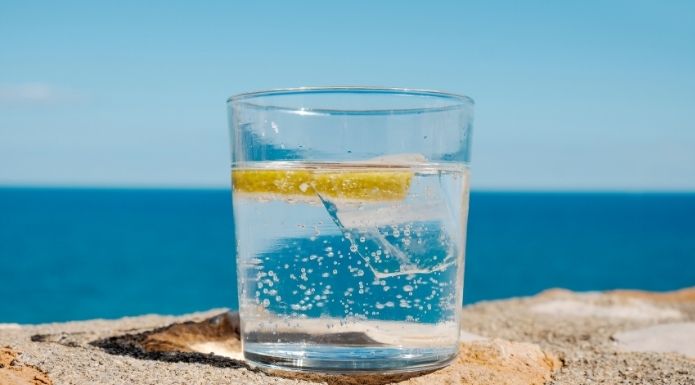 bubbly glass of Seltzer water with lemon and ice on the beach.