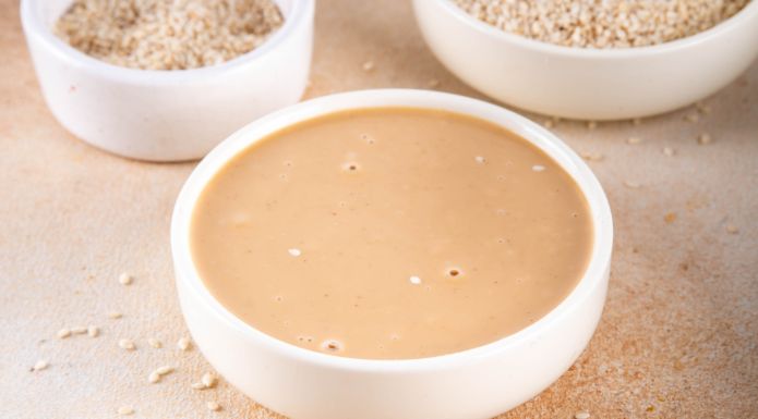 Tahini paste in bowl with sesame seeds in background