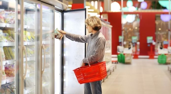 Young man scanning label of frozen food product at the supermarket, to illustrate the confusion over the term "fresh frozen." 
