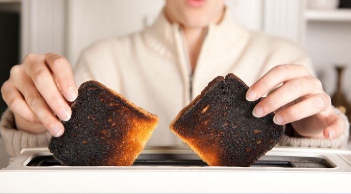 Two pieces of heavily burnt toast held in a person's hands, illustrating acrylamide exposure.
