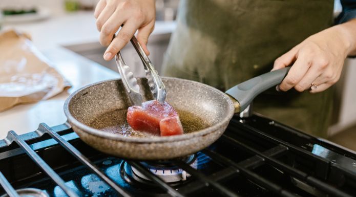 home cook using kitchen tongs to turn fish