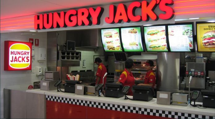Interior of Hungry Jack's restaurant location in Australia showing front counter, menu boards, and employees. 